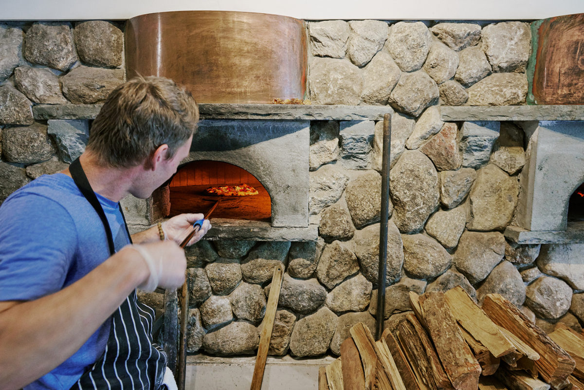person baking pizza at Fire & Stone Trattoria one of the best Restaurants and Takeout Options in Duxbury